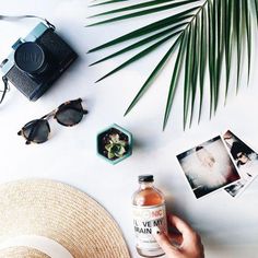 a person's hand holding a bottle of alcohol next to sunglasses and other items