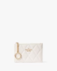 a small white purse with a gold chain hanging from the front, and a circular charm on