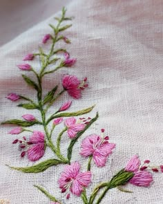 pink flowers are embroidered onto the side of a piece of linen with green stems on it