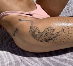 a woman laying on top of a bed with a tiger tattoo on her arm and leg