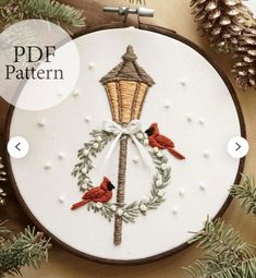 a cross stitch pattern with two birds and a lamp on it, surrounded by pine cones