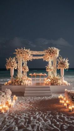 an outdoor wedding setup on the beach with candles and flowers in front of it at night