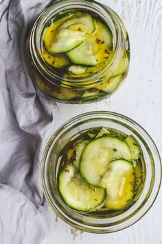 two jars filled with pickles on top of a white table cloth next to each other