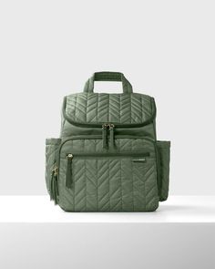 a green quilted backpack sitting on top of a white table next to a gray wall