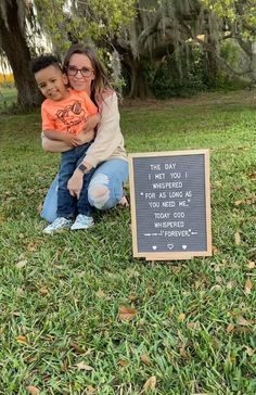 a woman and child sitting in the grass next to a sign