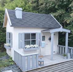 a small white house sitting on top of a wooden deck next to some green trees