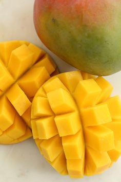 two pieces of mango sitting next to each other on a white counter top with one cut in half