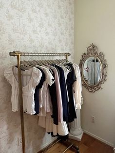 a rack with clothes hanging on it in front of a mirror and wallpapered wall