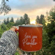 a person holding a red cup with the words love you pumpkin on it in front of some trees