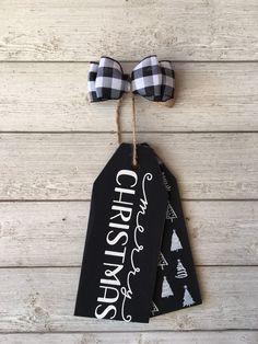 two black and white christmas gift tags with bows on them hanging from a wooden wall