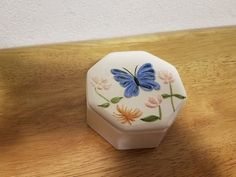 a white box with a blue butterfly painted on the lid sitting on top of a wooden table