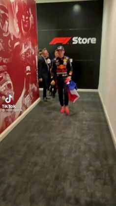 a man walking down a hallway next to a red and black wall with the store logo on it