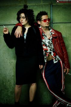 a man and woman standing next to each other in front of a wall wearing red sunglasses