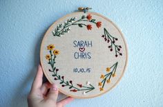 someone is holding up a cross stitch hoop with the name of their wedding date on it