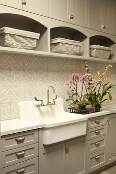 a white kitchen sink sitting next to a window filled with flowers and baskets on top of it