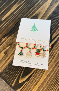 three christmas themed earrings sitting on top of a wooden table next to a greeting card