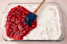 a red spatula sitting on top of a cake in a glass pan with white frosting