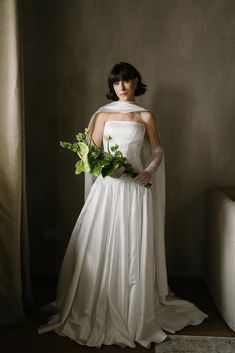 a woman in a white wedding dress holding a green bouquet and wearing a long veil