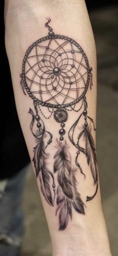 a woman's leg with a tattoo on it that has a dream catcher and feathers