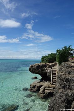 the water is crystal clear and blue with steps leading up to the cliff side area