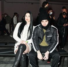 two people sitting on a bench in front of a crowd wearing black and white outfits