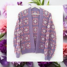 a purple knitted sweater sitting on top of a white board next to flowers and petals