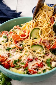 a blue bowl filled with pasta and veggies on top of a white table