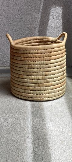 a large woven basket sitting on the floor next to a wall with a shadow cast on it