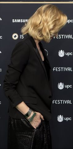 a woman in black jacket and pants standing next to a wall with the words festival on it