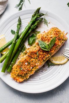 a white plate topped with fish next to asparagus and lemon wedged bread