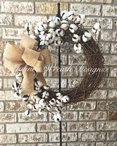 a wreath with cotton and a bow hanging on a pole in front of a brick wall