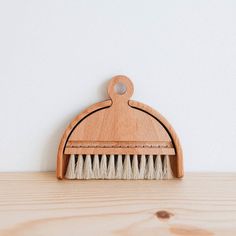 a wooden brush with white bristles sits on a wood surface next to a wall