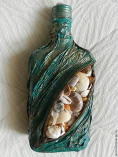 a bottle covered in shells sitting on top of a bed