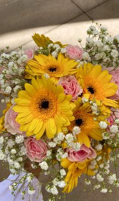 a bouquet of yellow and pink flowers in someone's hand on the ground,