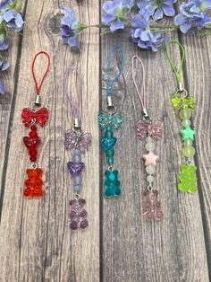 six different colored teddy bears are hanging from necklaces on a wooden table with purple flowers