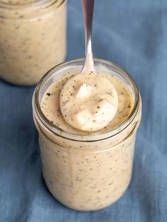 two jars filled with peanut butter on top of a blue tablecloth and one has a spoon in it