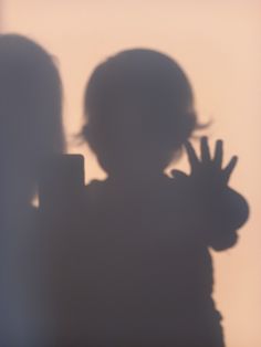 the shadow of a child holding his hand up in front of him and making a peace sign