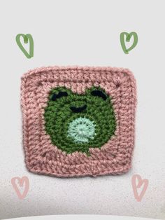 a crocheted square with a green face on it and hearts around the edges