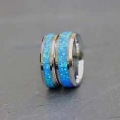 two wedding bands with blue opal and gold inlays are sitting on the ground