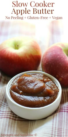 two apples sitting on top of a table next to a bowl of apple butter with the title slow cooker apple butter no peeling - gluten - free + vegan