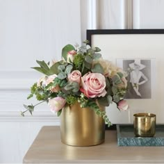 a gold vase filled with pink flowers on top of a table next to a candle