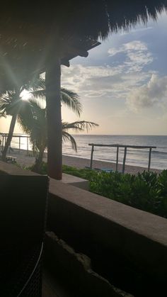 the sun is setting over the ocean with palm trees in front of it and a beach