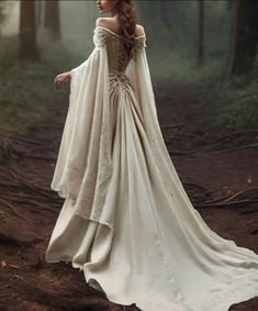 a woman in a white dress is walking through the woods with her arms around her back