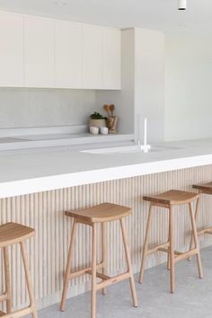 three wooden stools are sitting at the bar in this modern style kitchen with white cabinets