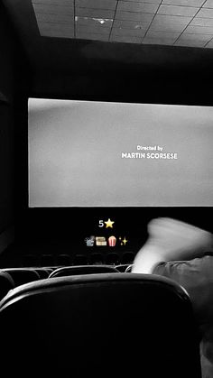 black and white photograph of a person sitting in front of a projector screen with the words martin scholak written on it