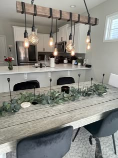 a dining room table with lights hanging from it's ceiling and greenery on top