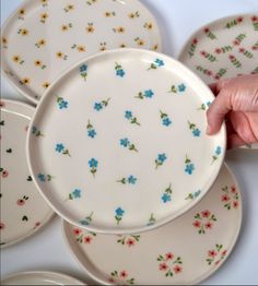 a hand is reaching for a plate with blue flowers on it, surrounded by other plates