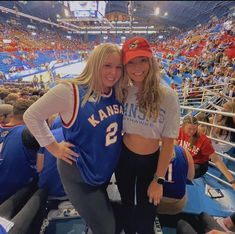 two women standing next to each other in front of an arena filled with people and fans