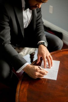 a man in a tuxedo sitting at a table signing something on a piece of paper