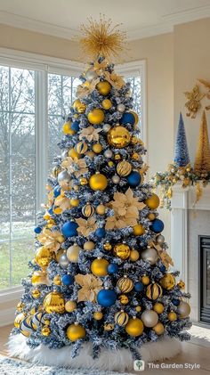 a blue and yellow christmas tree in a living room next to a window with gold ornaments